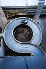 Spiral parking garage ramp with a car driving down, aerial view, urban infrastructure, modern city architecture, circular road design, transportation system, urban planning, industrial cityscape.