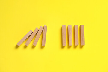 Domino effect. Wooden blocks on yellow background, flat lay