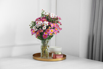 Beautiful flowers in vase and candles on white wooden table at home
