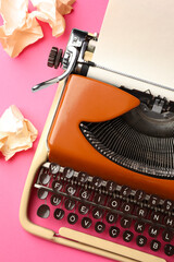 Vintage typewriter and crumpled paper on pink background, top view