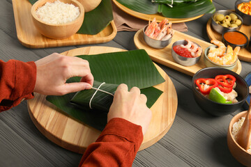 Woman tying banana leaf with food at wooden table with products, closeup. Healthy eco serving