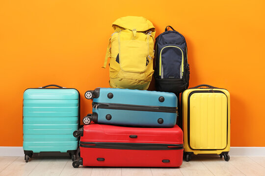 Many colorful suitcases and backpacks on floor near orange wall