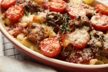 Delicious pasta casserole with cheese, tomatoes, minced meat and thyme in baking dish on table, closeup