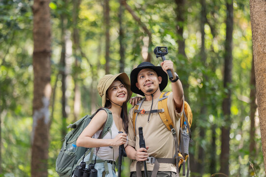 A travel blogger couple explores the forest, capturing stunning moments with their camera. They review photos together, documenting their adventure and sharing their experiences with the world.