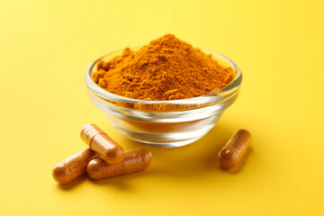 Turmeric powder in bowl and capsules on yellow background, closeup