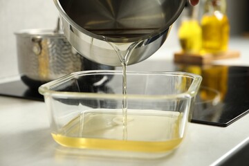 Pouring Used cooking oil into glass container at white countertop, closeup