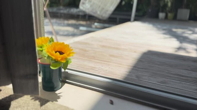 Sunflowers in a cup sitting bide a window to a wooden patio deck and green grass garden in Auckland, New Zealand.