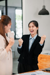 Two women in business attire celebrate a successful achievement in a modern office setting, expressing joy and excitement.