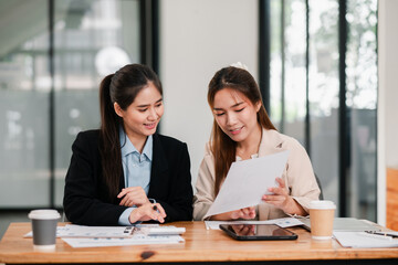 Two women engaged in a collaborative business meeting, reviewing documents in a modern office setting with natural light.