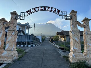 Beautiful rural view on the mountain slopes with Mount Merapi in the background. Village gate inscription "DK Stabelan"