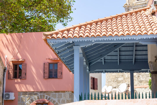 Combination architectural components including terracotta roof tiles,blue underside of veranda and pink plaster render outside wall