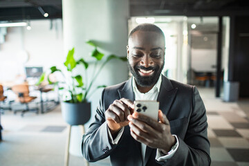 Smiling young black businessman using smartphone in modern office