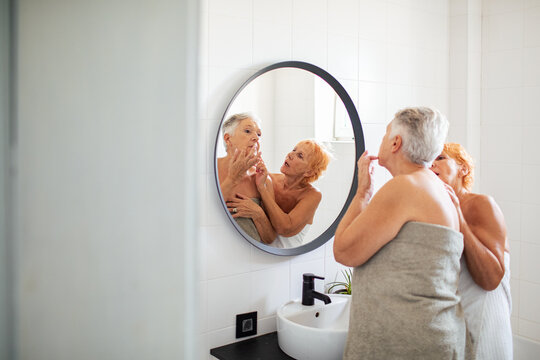 Senior lesbian couple looking at mirror in bathroom after shower - Powered by Adobe