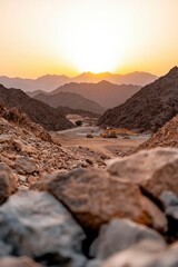 Obraz premium Construction equipment sits in a desert valley at sunset, rocky foreground