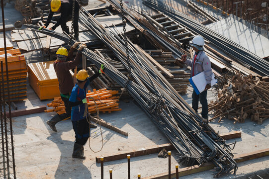 Construction Workers Handling Steel Rebar, Workers are skillfully maneuvering steel rebar on construction site, teamwork and safety in bustling environment of building infrastructure