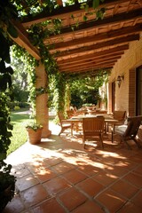 Fototapeta premium Outdoor patio with table & chairs, covered by vines. Garden in background
