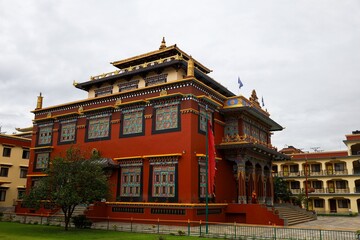 Obraz premium Traditional Tibetan architecture of Shechen Monastery in Boudha, Kathmandu, Nepal, with vibrant red walls and intricate gold details, set against a cloudy sky in Kathmandu Valley.