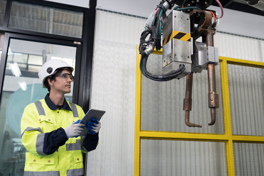 Male engineer using digital tablet control automatic robotic hand machine welding in building room workshop. Male technician worker working with control automatic robot arm system welding