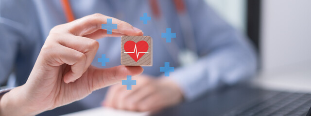 Professional healthcare medical worker holding red heart with cardiogram on wooden block...