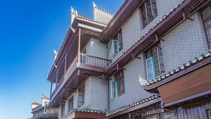Chinese architecture. A fragment of a brick apartment building. Windows on the facade, balconies with railings, roofs with curved cornices. The blue sky. China. Fenghuang.