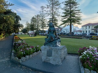 Bronze statue of Pania of the Reef, a M?ori legend, sits in a park. Picnic-goers relax nearby. Napier Hill, Napier, Hawke's Bay, New Zealand