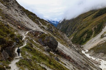 A trekker walks along a rugged trail towards Kanchenjunga Base Camp, surrounded by dramatic peaks and valleys in the Nepalese Himalayas.s