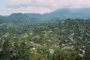 Panoramic view of green hills and scattered houses under cloudy sky, showing peaceful countryside...