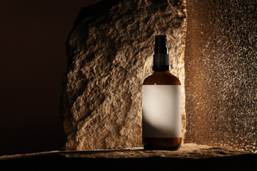 Amber glass spray bottle with a blank label, placed on natural stone and highlighted by moody,...