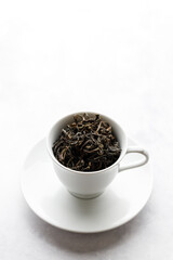 Cup of hot tea filled with tea leaf on white table background.