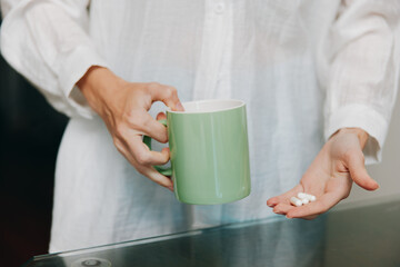 Woman holding green coffee mug and white pill in hands