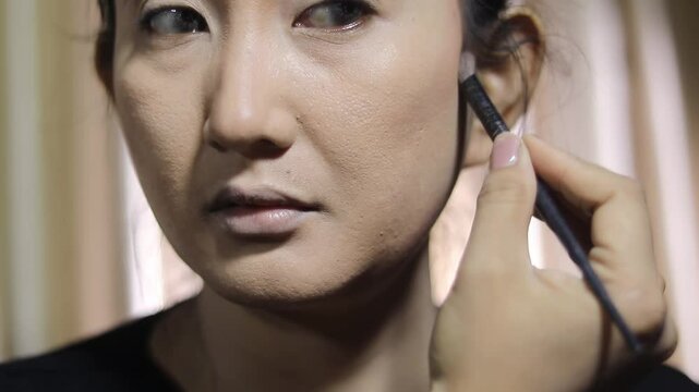 A woman is shown with the foundation process. Close-up of a face being prepared with foundation, using a brush for makeup and skin tone.