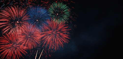 Fototapeta premium Fireworks in a mix of red, blue, and green against a pitch-black sky, with a wide open space of darkness on the right, ideal for banners.