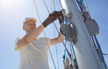 Male captain on deck of sailboat opening sails pulling the rope
