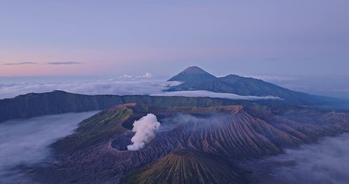 aerial view of breathtaking Mount Bromo surrounded by mist and dramatic landscapes. an active volcano in Indonesia, The soft morning light highlights the rugged terrain and the rising volcanic smoke