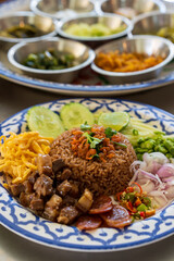 dried shrimp paste fried rice mixed with sausage egg or chopped omelet fresh chili long beans onion mango cucumber lemon and sweet streaky pork in plate with side dishes tray on table by thai food