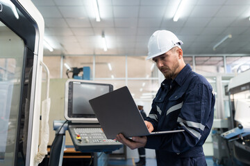 Male engineer working with laptop computer for control machine in factory. Male factory worker working with lathe machine with safety uniform and helmet in factory