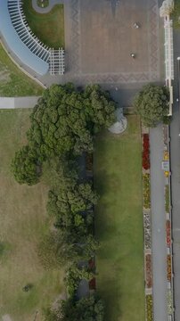 Aerial view of a meticulously landscaped park. Circular flowerbeds and pathways create a beautiful design. A tractor is visible in the lower left. Sunken Gardens, Napier, Hawkes Bay, New Zealand