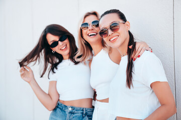 Three young beautiful smiling hipster female in trendy summer white t-shirt  and jeans clothes. Sexy carefree women posing in street. Positive models having fun, going crazy. In sunny day, sunglasses