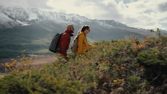Two young active hikers with backpacks are going uphill in mountains