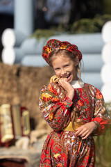 A blonde girl in a national Russian costume on the Maslenitsa holiday. A beautiful russian girl in a national costume made of a fur cape and kokoshnik on the background of a hayloft. 