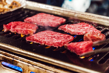 Marbled wagyu beef sizzling on yakiniku grill over an open flame at a Japanese barbecue restaurant. Rich texture, high-quality meat highlight gourmet dining, authentic Japanese cuisine. Tokyo, Japan
