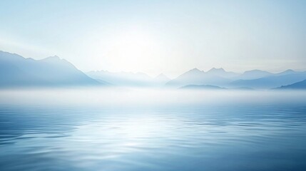 Serene misty mountain landscape with calm water reflections under a bright sky
