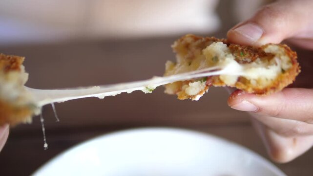 Hand breaking a crispy cheese croquette showing stretchy melted cheese inside