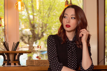 Stylish woman in retro polka dot blouse sitting at a cozy cafe table with a thoughtful expression