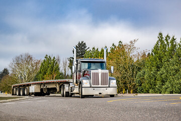 Stylish black bonnet big rig semi truck transporting empty flat bed semi trailer running on the...