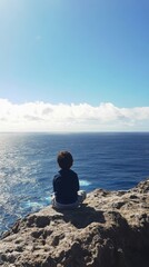 Fototapeta premium Child enjoying a serene moment by the ocean on a rocky cliff in summer sun