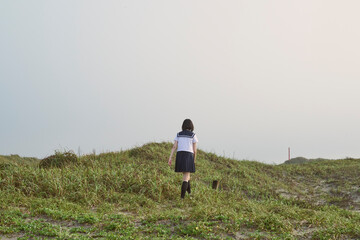 草原に立つ女子高校生の後ろ姿