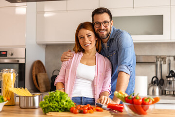 Portrait of happy young couple cooking together in the kitchen at home. romantic Attractive young woman and handsome man are enjoying spending time together while standing on light modern kitchen.