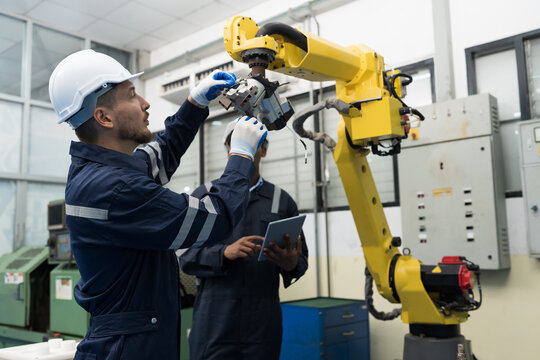 Two male engineer maintenance automatic robotic arm in workroom of building. Group of male technician checking and inspecting quality of automatic robot arm by tablet
