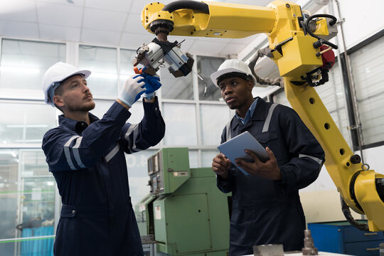 Two male engineer maintenance automatic robotic arm in workroom of building. Group of male technician checking and inspecting quality of automatic robot arm by tablet